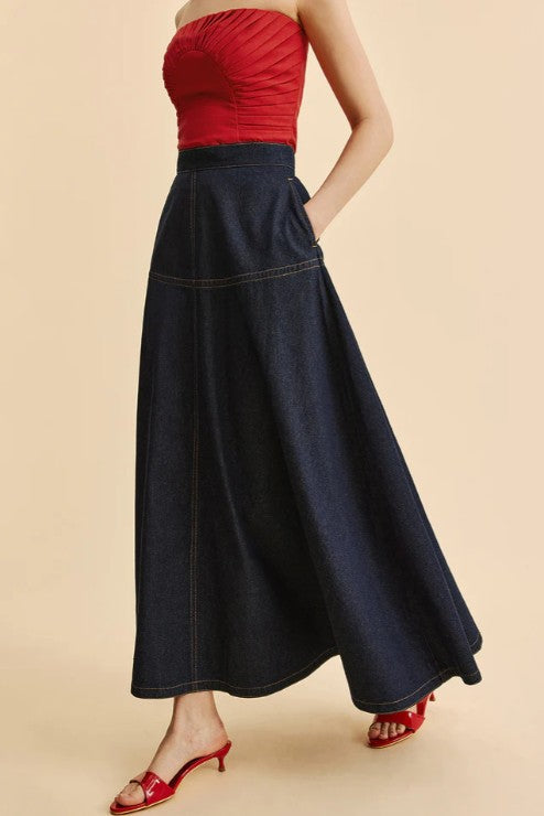 Person wearing a red top and long navy skirt on a beige background