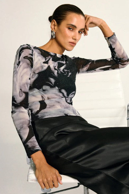 Woman wearing a black and white patterned top sitting on a chair.