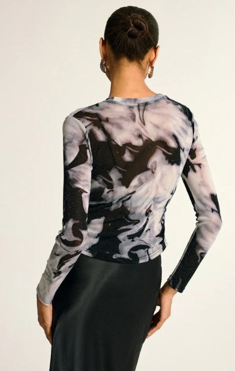 Person wearing a long-sleeve, abstract patterned top with a plain background