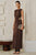 Woman in a brown dress holding a clutch against a neutral wall.