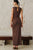 Woman wearing a brown dress standing in a minimalistic room with a bench and wall.