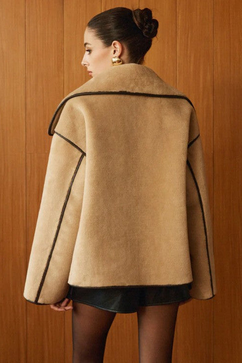 Woman wearing a beige coat with brown trim against a wooden background