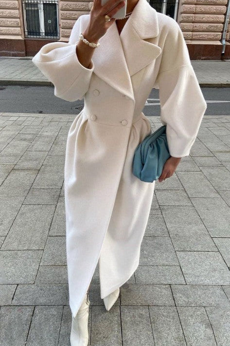 Person wearing a white coat holding a blue clutch on a sidewalk.