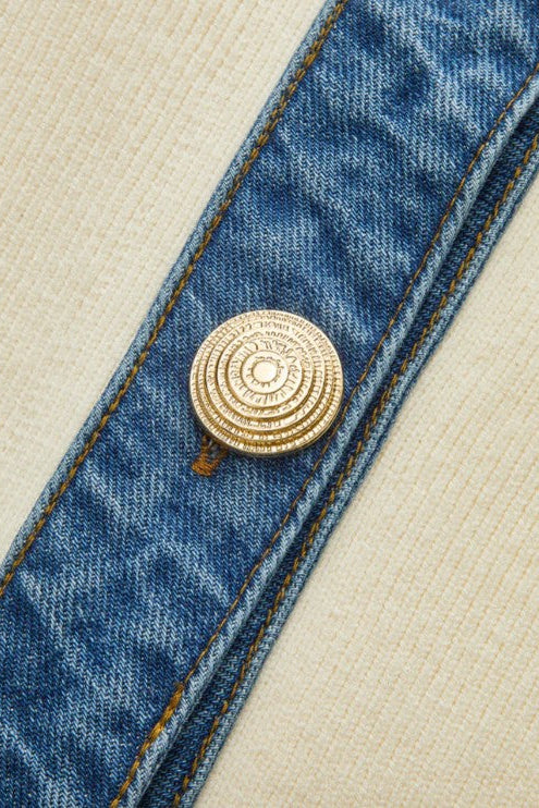 Close-up of a blue denim strap with a gold button on a beige background