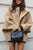 Person wearing a beige coat holding a black quilted handbag against a light background