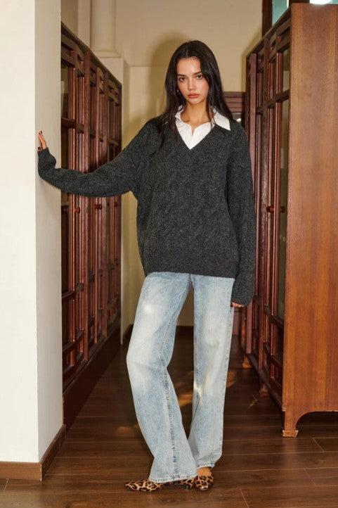 Woman wearing a dark gray sweater and light blue jeans standing in a library.