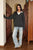 Woman wearing a dark gray sweater and light blue jeans standing in a library.