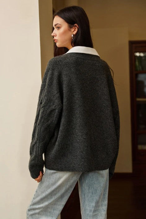 Person wearing a dark gray sweater with a white collar indoors.