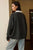 Person wearing a dark gray sweater with a white collar indoors.