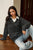 Woman wearing a dark gray sweater over a white shirt and light blue jeans, sitting on a wooden floor.