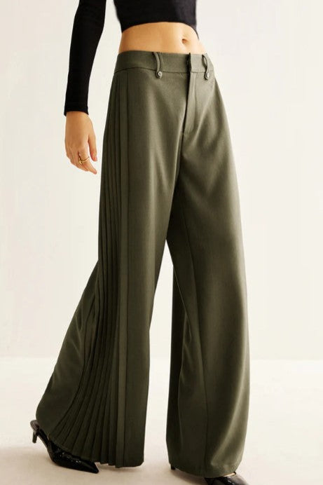 Green pleated pants worn by a person on a plain background